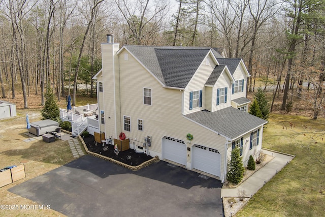 view of side of property with driveway, an outdoor structure, a shingled roof, a garage, and a chimney