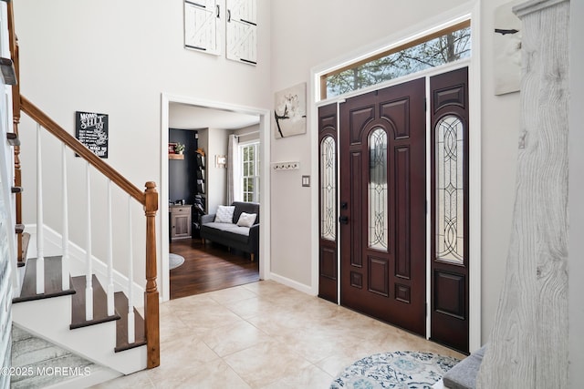 foyer entrance featuring stairway, baseboards, a towering ceiling, and tile patterned flooring