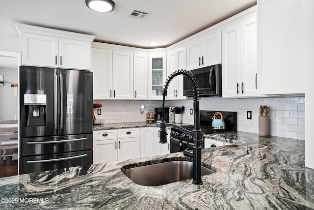 kitchen with black gas range oven, visible vents, dark stone counters, white cabinetry, and stainless steel fridge