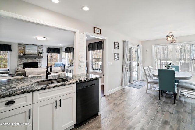 kitchen with a sink, dark stone countertops, black dishwasher, light wood-style floors, and a fireplace