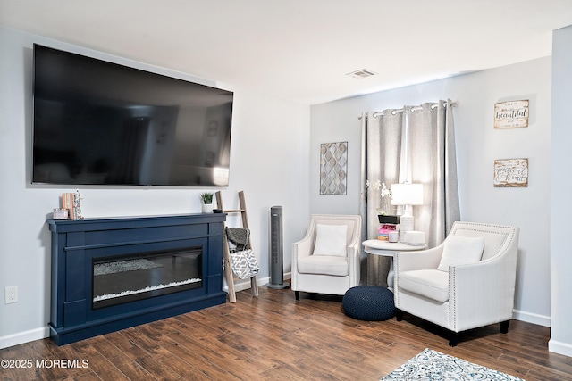 sitting room featuring a glass covered fireplace, wood finished floors, visible vents, and baseboards