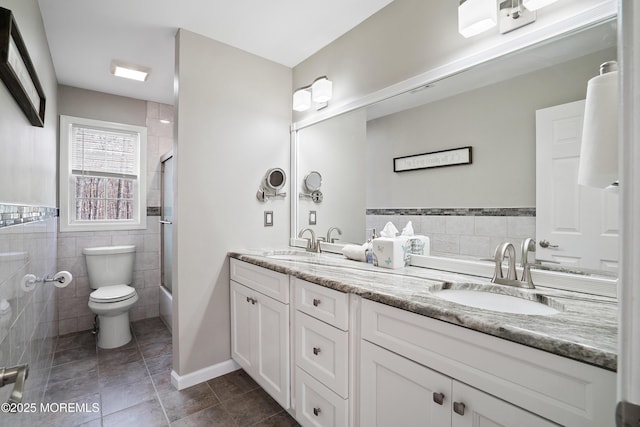 bathroom with double vanity, toilet, tile walls, and a sink