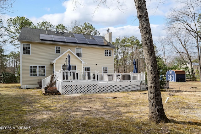 rear view of house featuring an outbuilding, roof mounted solar panels, a storage shed, a wooden deck, and a chimney