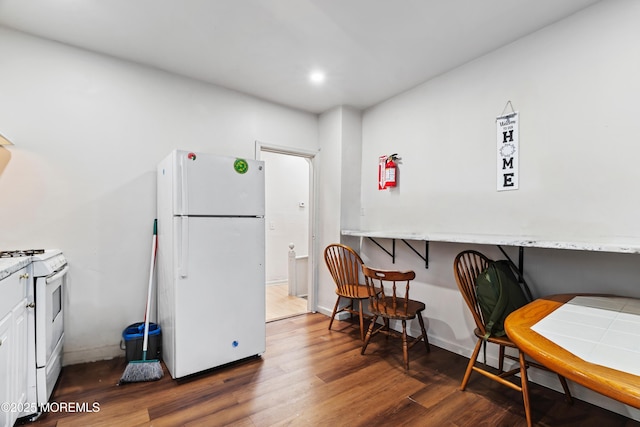 kitchen featuring recessed lighting, white appliances, wood finished floors, white cabinetry, and a kitchen bar