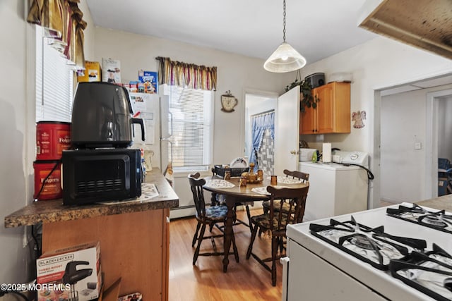 kitchen with white range with gas stovetop, hanging light fixtures, brown cabinetry, light wood finished floors, and washer and clothes dryer