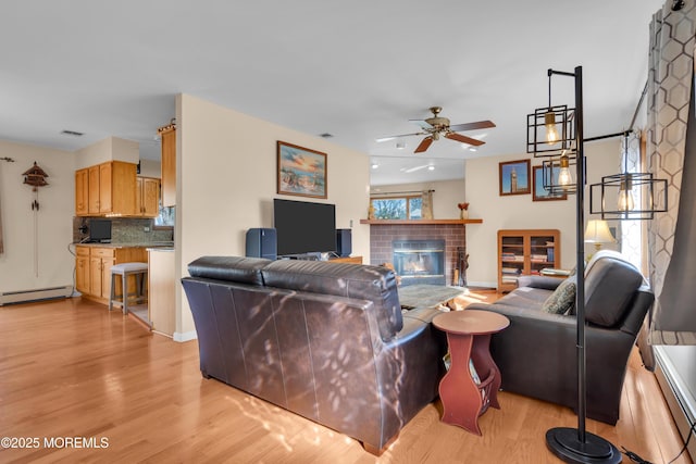 living room with light wood-type flooring, ceiling fan, a fireplace, and a baseboard radiator