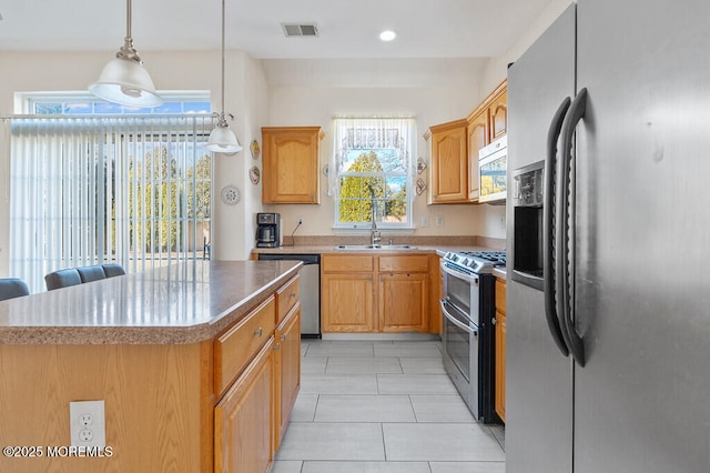 kitchen with stainless steel appliances, a sink, visible vents, a center island, and decorative light fixtures