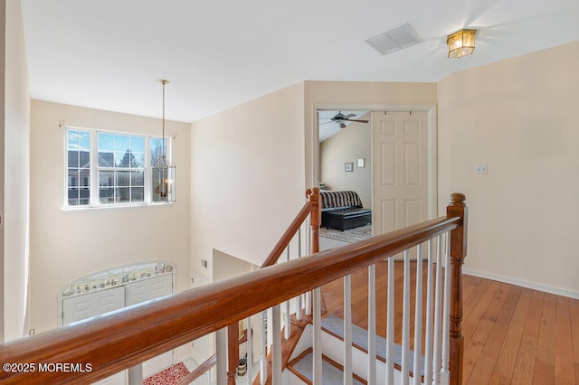 hallway featuring light wood-type flooring, baseboards, a notable chandelier, and an upstairs landing