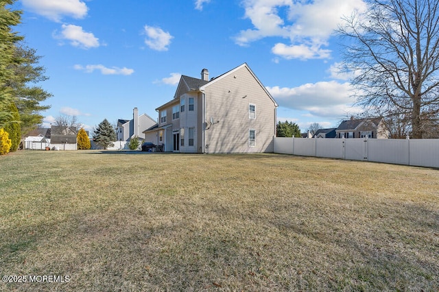 back of house featuring a yard, fence, and a chimney