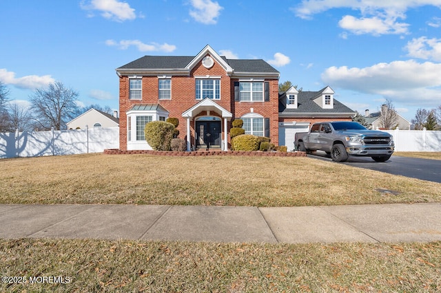 colonial house with brick siding, concrete driveway, a front yard, fence, and a garage