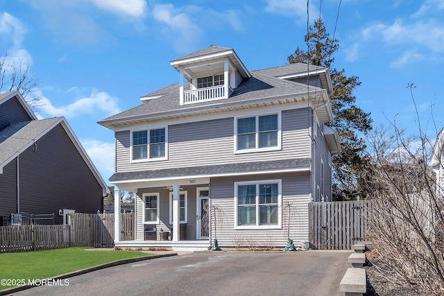 traditional style home with a balcony, covered porch, a shingled roof, fence, and driveway