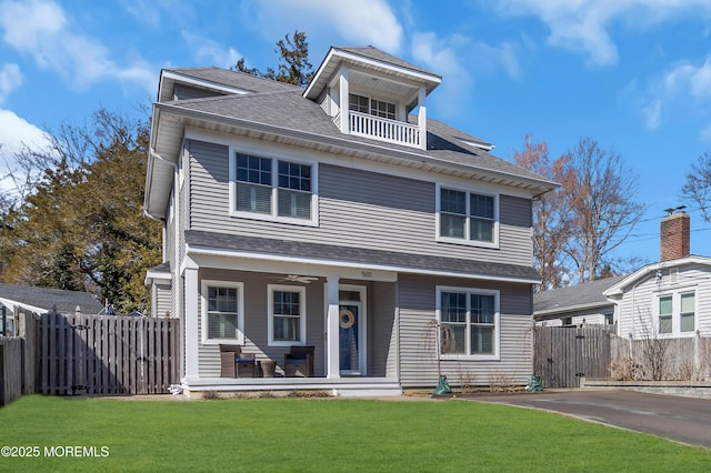 american foursquare style home featuring a porch, a balcony, a shingled roof, fence, and a front yard