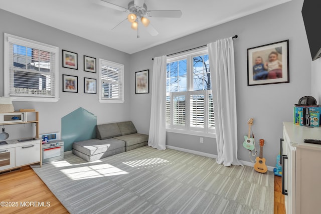 living area featuring a ceiling fan, light wood-type flooring, visible vents, and baseboards