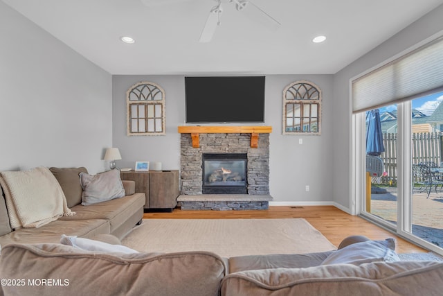 living area featuring recessed lighting, a stone fireplace, baseboards, and wood finished floors