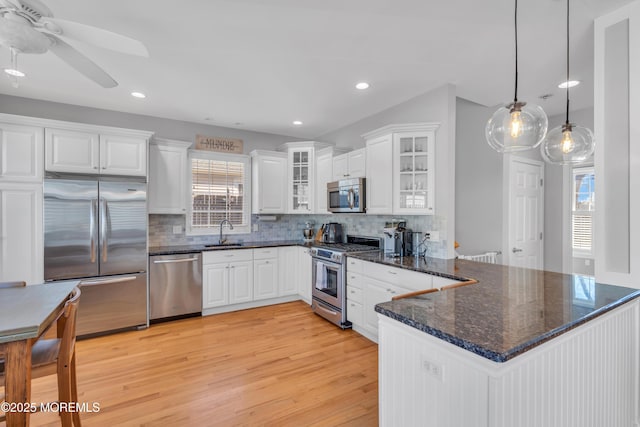 kitchen with a peninsula, a sink, white cabinetry, appliances with stainless steel finishes, and tasteful backsplash