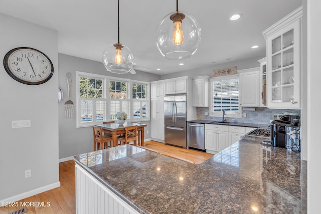 kitchen featuring light wood-style flooring, a sink, white cabinets, appliances with stainless steel finishes, and tasteful backsplash