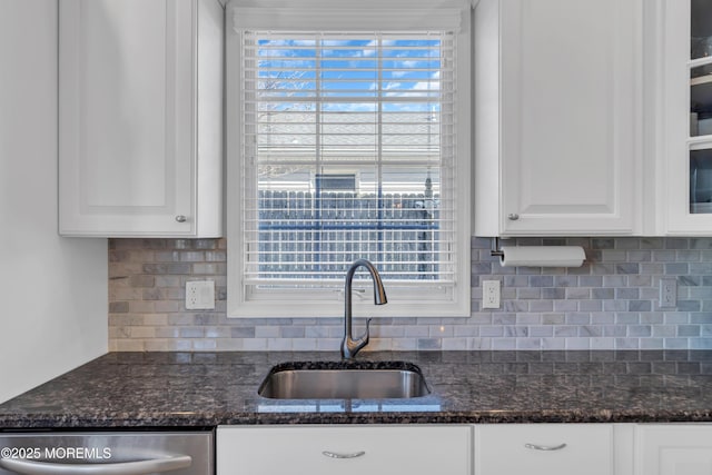 kitchen with dishwasher, glass insert cabinets, dark stone countertops, white cabinetry, and a sink