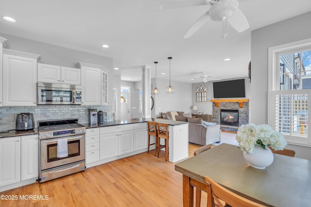 kitchen featuring light wood finished floors, white cabinets, decorative backsplash, ceiling fan, and appliances with stainless steel finishes