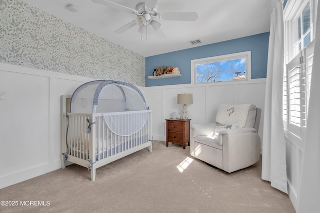 bedroom featuring a decorative wall, visible vents, wainscoting, carpet, and wallpapered walls