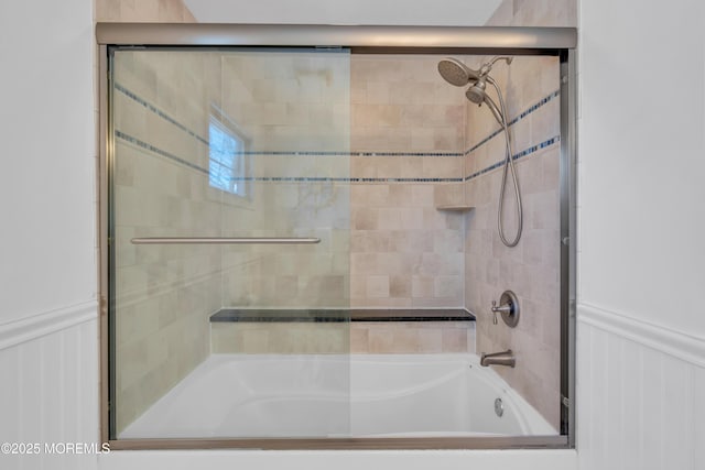 bathroom with a wainscoted wall and bath / shower combo with glass door