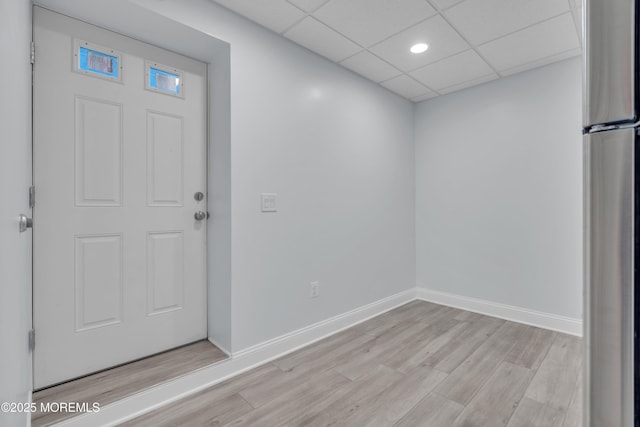 foyer entrance featuring light wood finished floors, a paneled ceiling, and baseboards