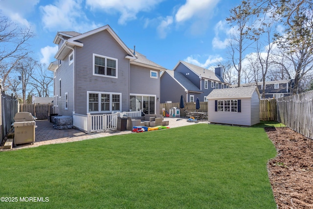 rear view of property featuring a patio area, a lawn, an outdoor structure, and a fenced backyard