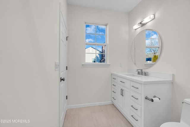 bathroom featuring baseboards, vanity, toilet, and a healthy amount of sunlight