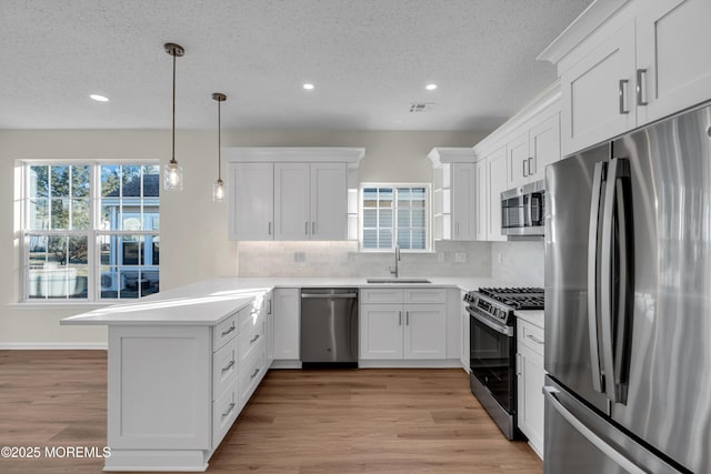 kitchen with stainless steel appliances, a peninsula, a sink, visible vents, and white cabinets