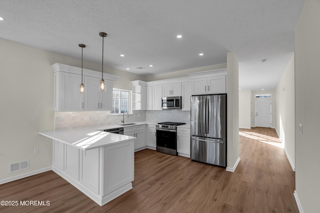 kitchen featuring a peninsula, a sink, visible vents, white cabinetry, and appliances with stainless steel finishes