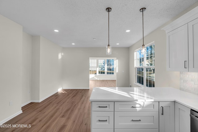 kitchen with decorative light fixtures, light countertops, white cabinetry, light wood-type flooring, and a peninsula