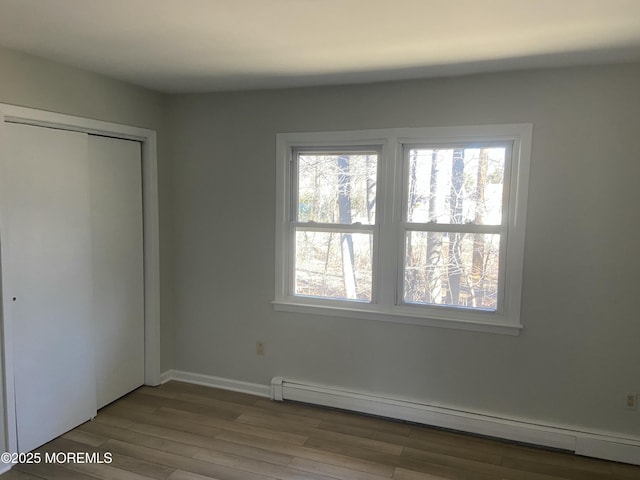 unfurnished bedroom with a closet, baseboards, baseboard heating, and wood finished floors