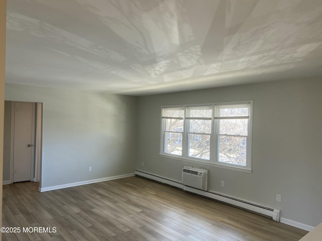 unfurnished room with a baseboard radiator, wood finished floors, and baseboards