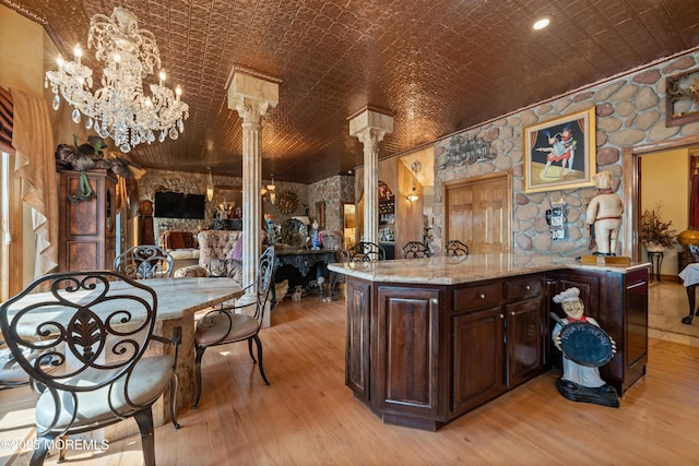 kitchen with light wood-style flooring, an ornate ceiling, open floor plan, dark brown cabinetry, and decorative columns