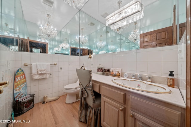 bathroom with a notable chandelier, toilet, a sink, wood finished floors, and tile walls