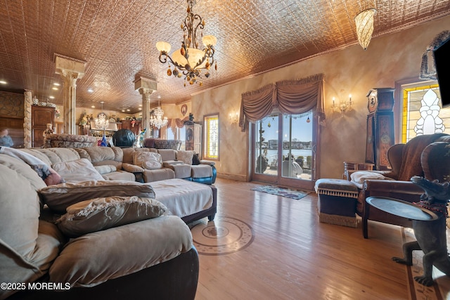 living area featuring wood finished floors, ornate columns, an inviting chandelier, an ornate ceiling, and crown molding