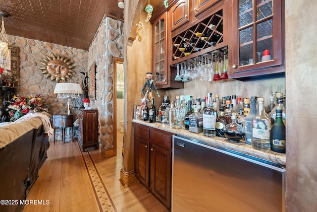 bar with a bar, refrigerator, and light wood-style floors