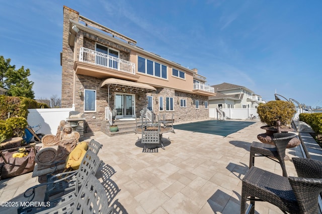 rear view of house with stone siding, a fenced backyard, french doors, a balcony, and a patio area