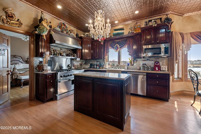 kitchen featuring an ornate ceiling, stainless steel appliances, an inviting chandelier, wall chimney exhaust hood, and crown molding