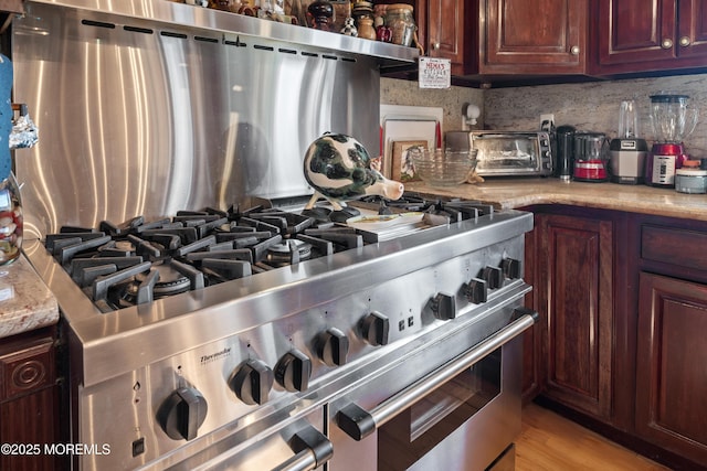 kitchen with light wood-type flooring, light stone counters, tasteful backsplash, a toaster, and range with two ovens