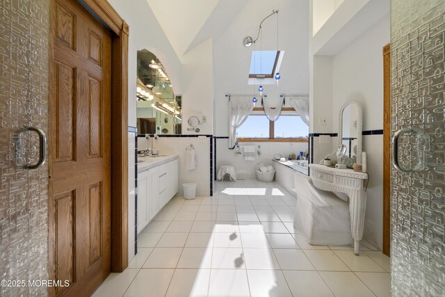 full bathroom with tile patterned flooring, tile walls, vaulted ceiling with skylight, and a wainscoted wall