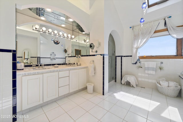 bathroom featuring double vanity, a sink, tile patterned flooring, wainscoting, and tile walls