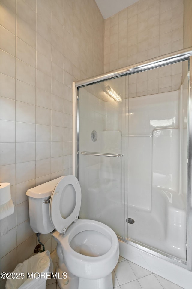 full bath with a shower stall, toilet, tile walls, and tile patterned floors