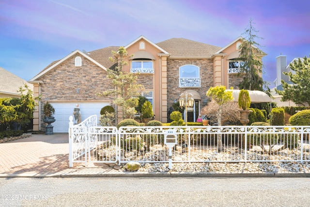 view of front of home with a fenced front yard, roof with shingles, decorative driveway, a garage, and stone siding