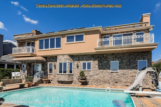 rear view of property featuring stucco siding, an outdoor pool, a chimney, and a balcony