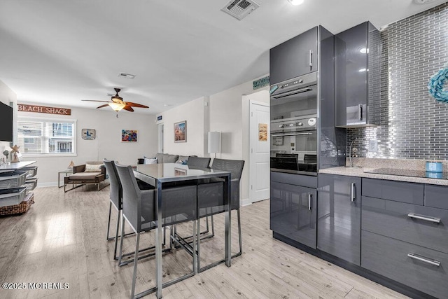 kitchen featuring visible vents, light wood-type flooring, backsplash, and oven