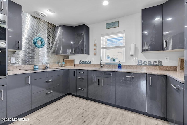 kitchen with light wood finished floors, visible vents, decorative backsplash, a sink, and black electric cooktop