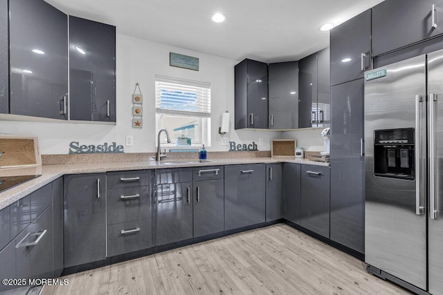 kitchen with light wood-style flooring, modern cabinets, high end fridge, light stone countertops, and a sink