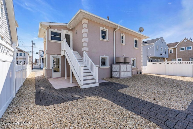 back of house with a fenced backyard, a patio, stairway, and stucco siding