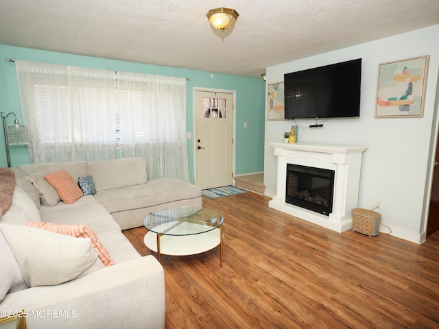 living room with a glass covered fireplace, a textured ceiling, baseboards, and wood finished floors