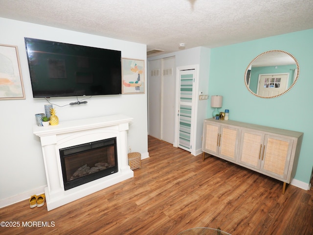 living area featuring a glass covered fireplace, a textured ceiling, baseboards, and wood finished floors